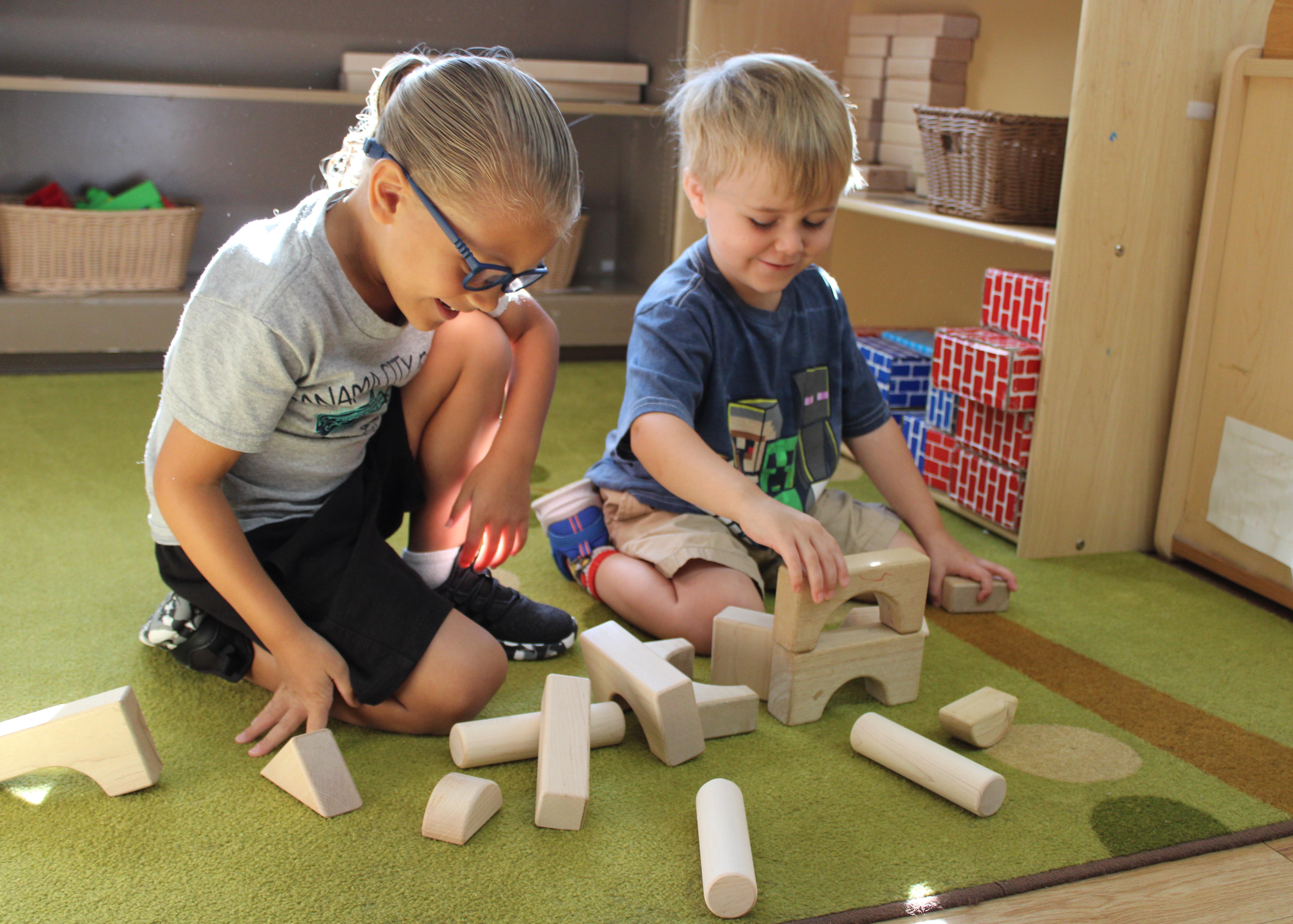 A boy and a girl play with building blocks on the floor of a Head Start classroom